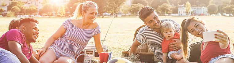 Adults and children have a picnic on a blanket in a field of grass.