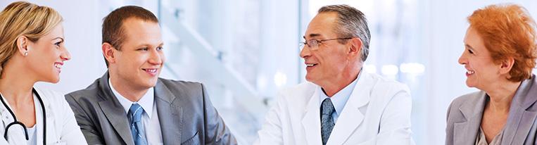 Two health care providers and two people in business suits sit around a table and talk.