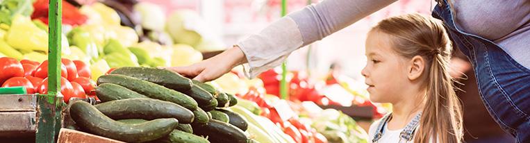 A pregnant mother and her young daughter look at cucumbers in the produce section of a supermarket.