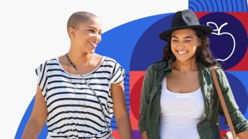 Two young women smile and laugh while walking together.