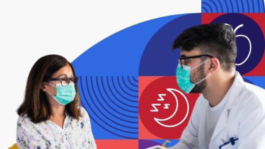 An older woman wearing glasses and a face mask sits across from her healthcare provider while they talk. 